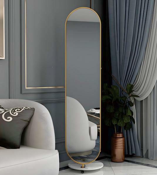 Full-length mirror with gold frame on a stand in a living room setting.