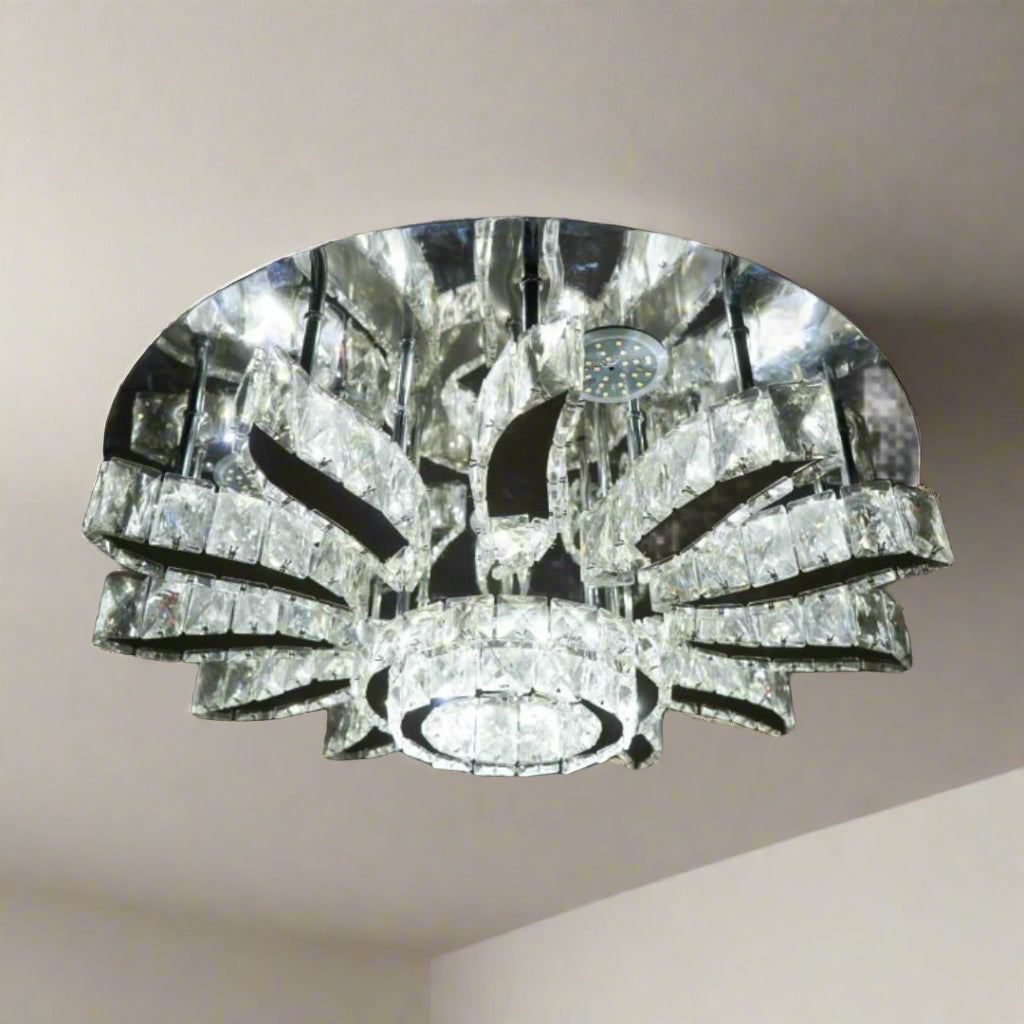 A grand round chandelier with multiple outward-bending arms made of clear crystal, forming a radial pattern and suspended from a dark ceiling; it gives off cool white lighting and adds dramatic flair to large spaces.