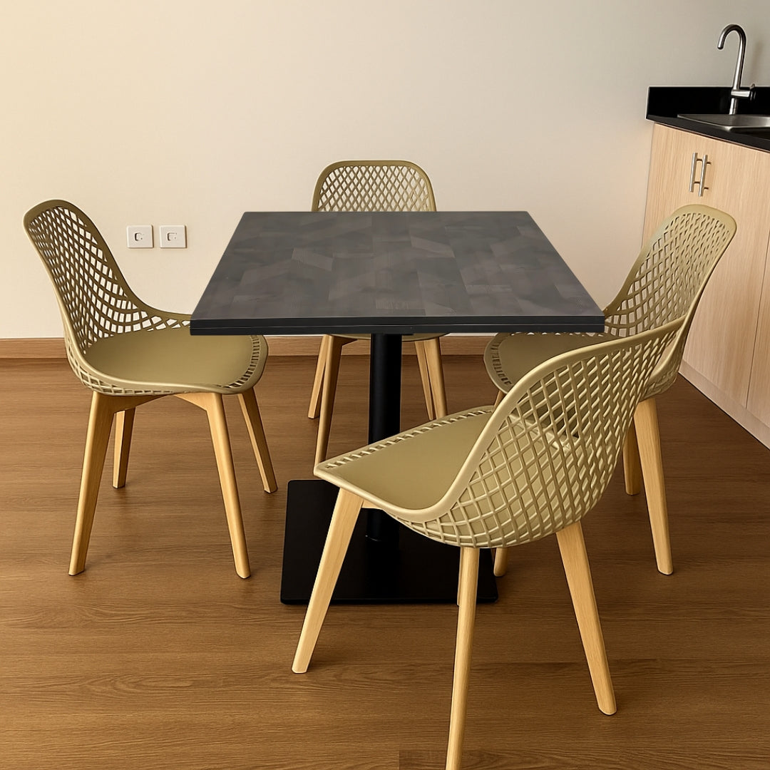 Four chairs with woven backs around a square table in a room with wooden flooring and a kitchen area.
