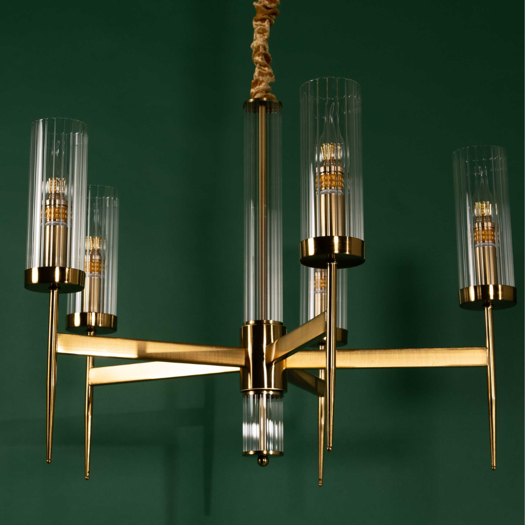Metal chandelier with symmetrical geometric arms and vertical glass shades against a green wall backdrop.