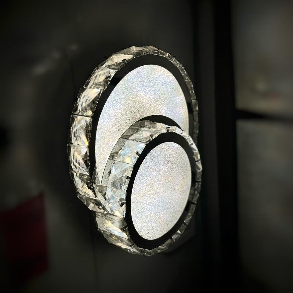 A set of three overlapping circular LED wall lights with crystal detailing, mounted on a dark wall.