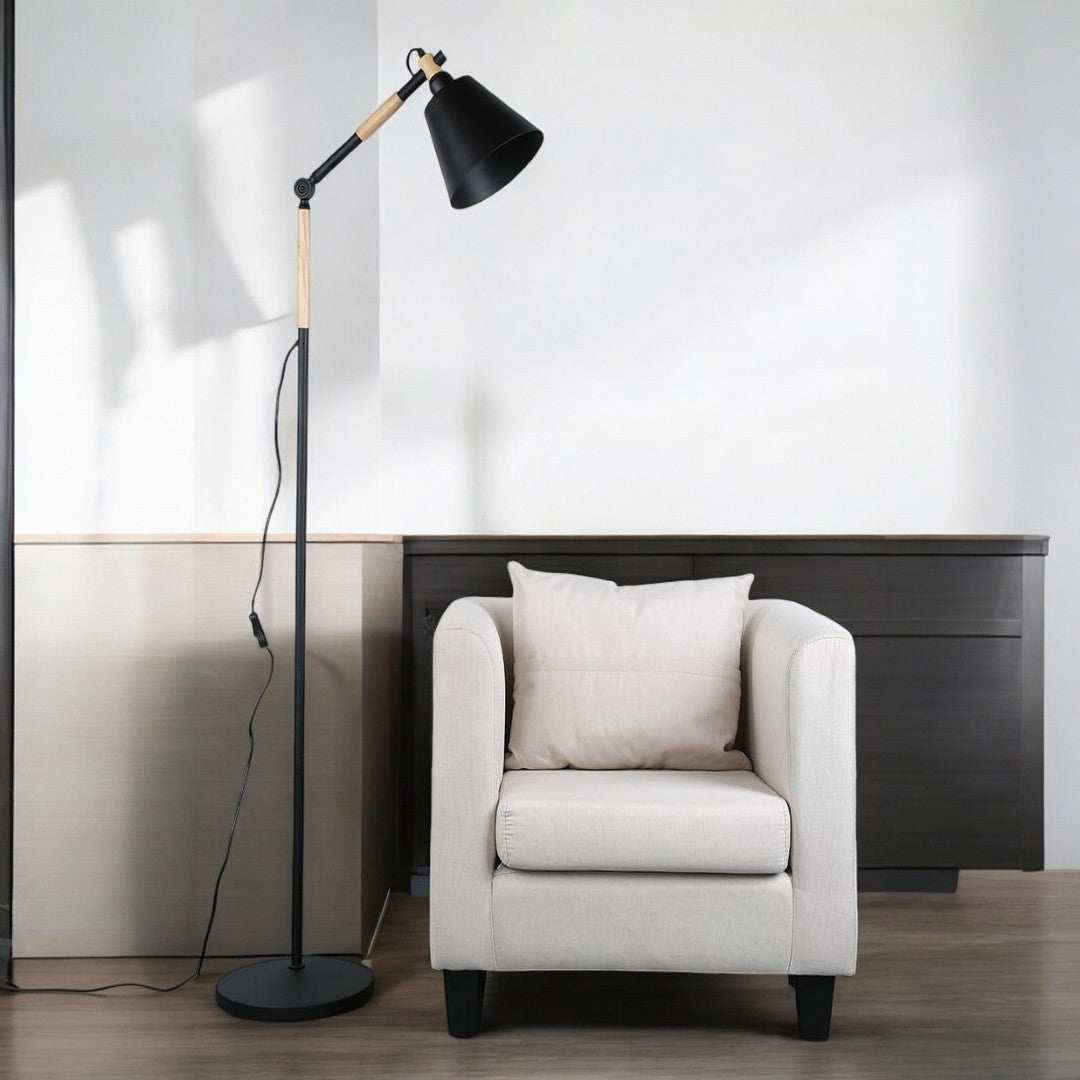 A modern black floor lamp with an adjustable head, placed beside a white armchair in a minimalistic living room.