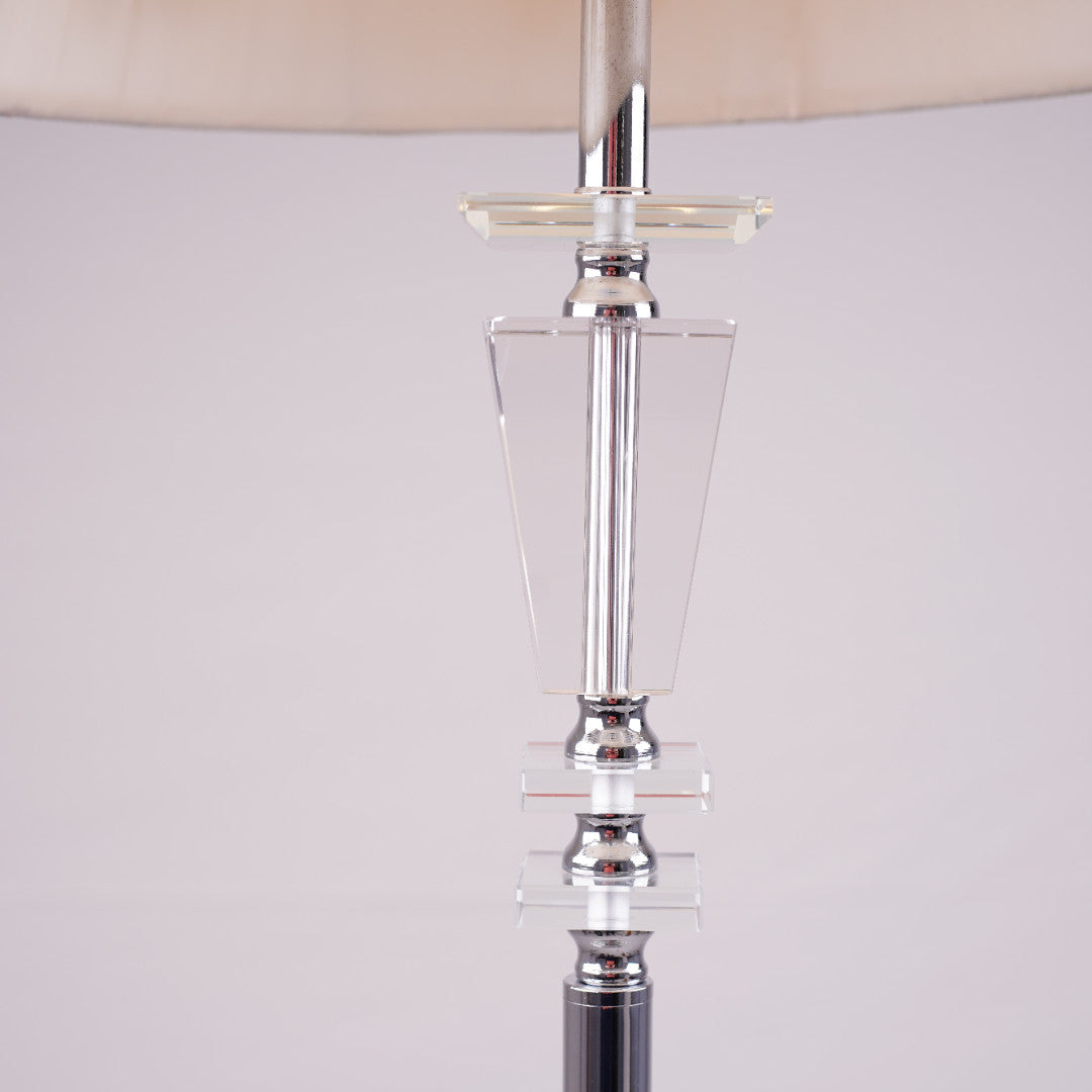 Tall modern floor lamp with a sleek glass and chrome base, placed in a minimalistic setting.