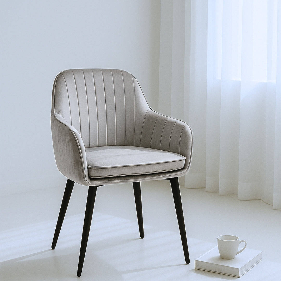 Gray upholstered chair with black legs in a bright room with white curtains.