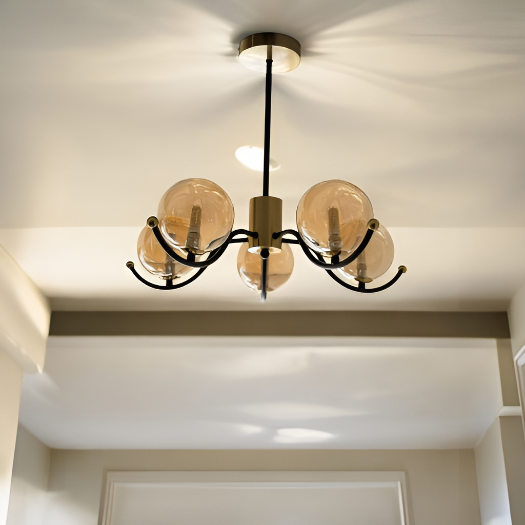 A modern chandelier with a golden base, black arms, and five glass globe bulbs, mounted on a white ceiling.