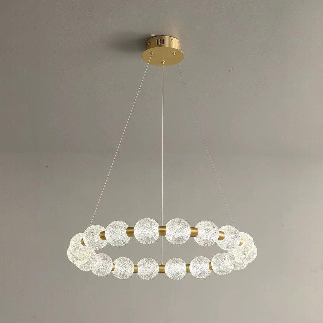 A contemporary circular chandelier with frosted spherical glass shades arranged in a ring, suspended by thin wires from a gold ceiling mount.