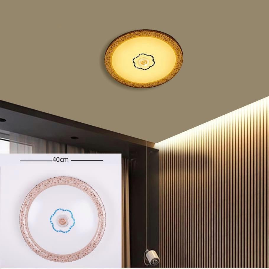 A circular flush ceiling light with a soft golden border and a small central floral detail, installed on a beige ceiling near wood paneling; it emits a cozy, warm yellow light and is about 40 cm in diameter.