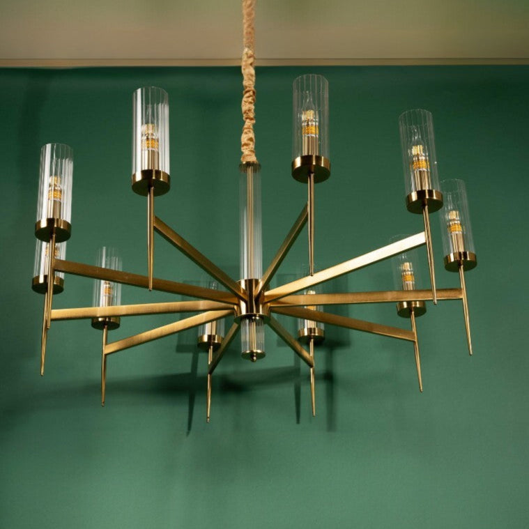 Metal chandelier with symmetrical geometric arms and vertical glass shades against a green wall backdrop.