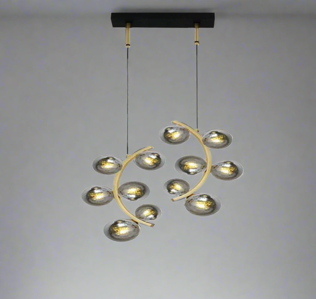 Modern decorative ceiling light fixture with two symmetrical, curved golden arms, each holding six metallic, oval-shaped lamp covers resembling flower petals or spoons. The fixture hangs from a black rectangular base via two thin cables against a plain gray background.