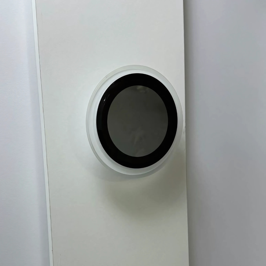 Unlit circular wall-mounted LED light with a sleek black center and white rim, blending into a minimalist white wall background.