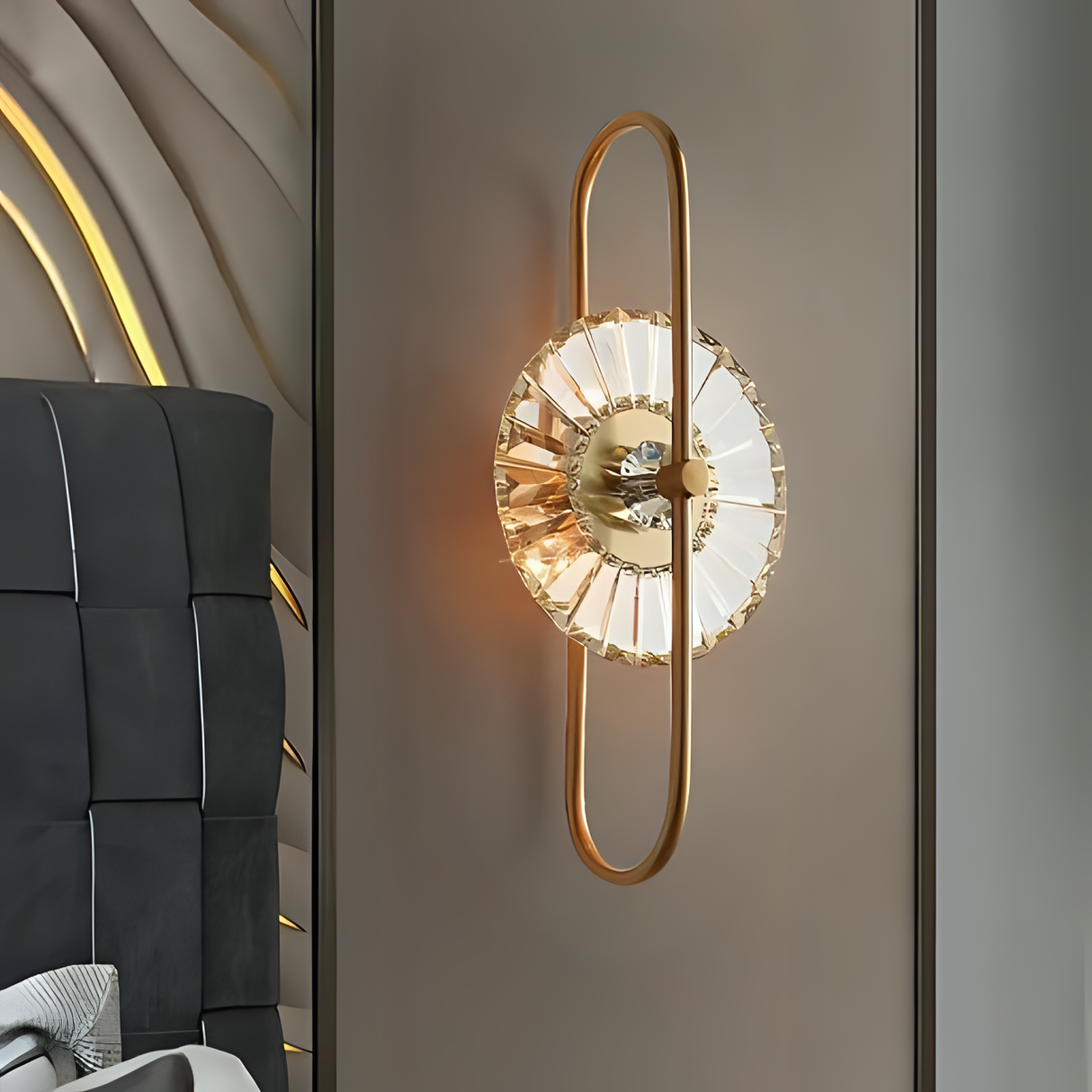 A modern gold wall sconce featuring an elongated oval frame with a central textured glass element, casting a soft, radiant glow.