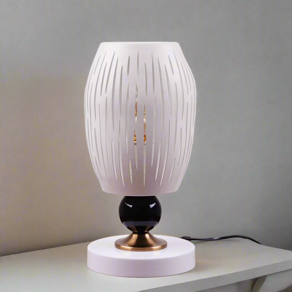 A white globe table lamp with a geometric design, gold accents, and a sleek base sits on a wooden table. It features an LED light with an E27 bulb, casting a warm, stylish glow.