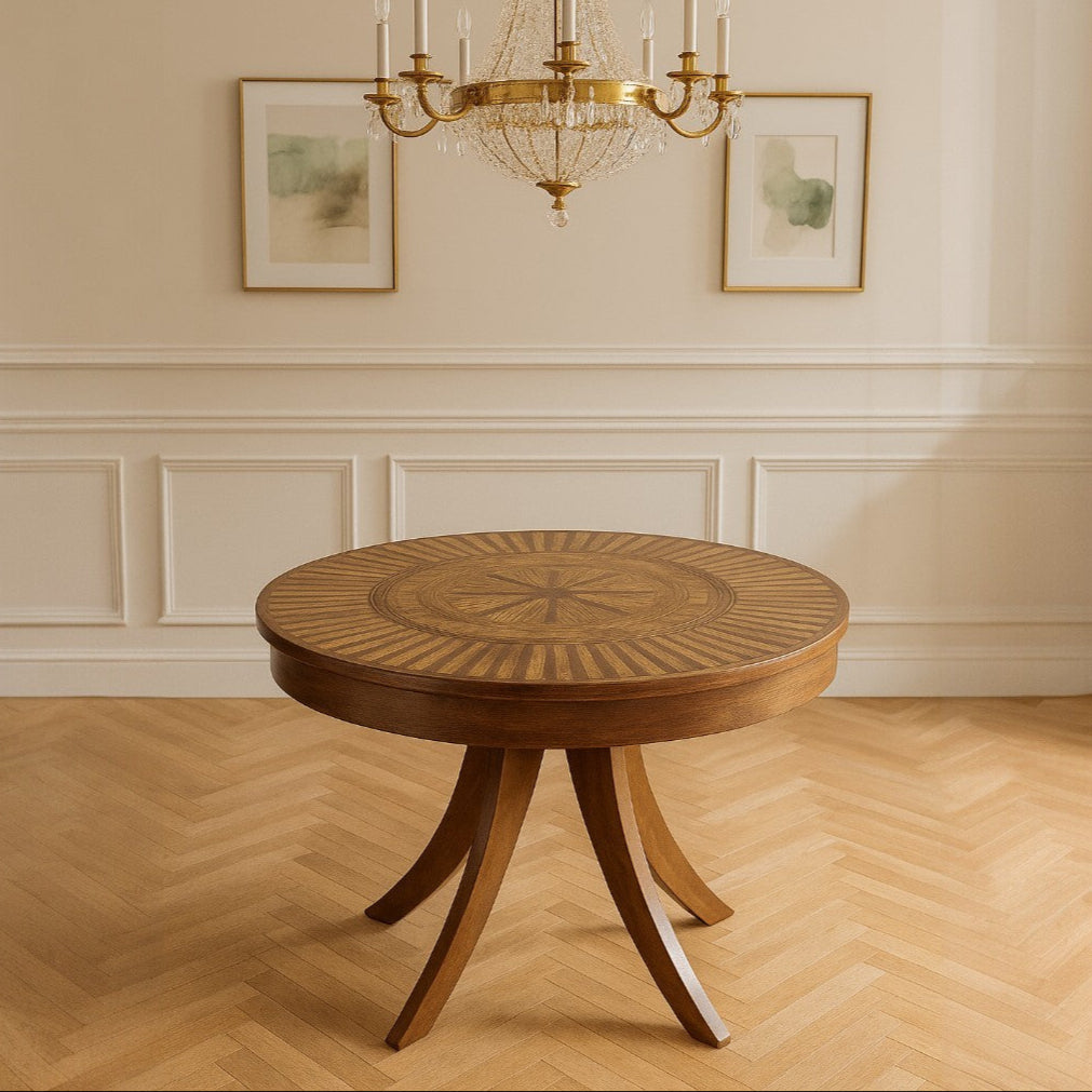 Round wooden table in a room with a chandelier and framed pictures on the wall.