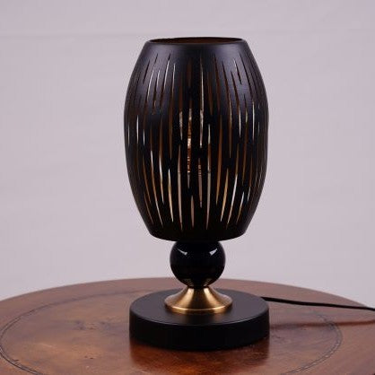 A black globe table lamp with a geometric design, gold accents, and a sleek base sits on a wooden table. It features an LED light with an E27 bulb, casting a warm, stylish glow.