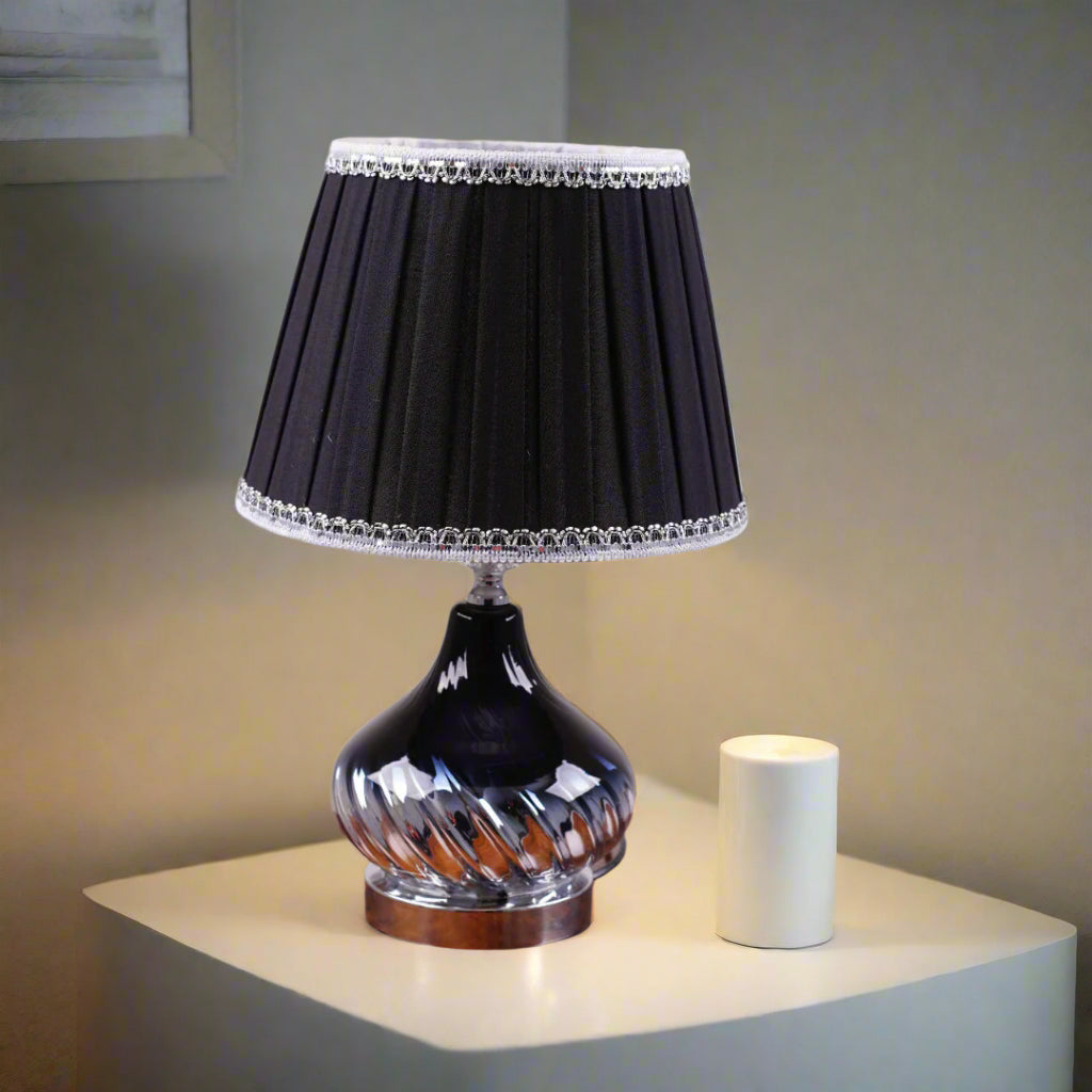 An elegant table lamp with a chic twisted silver base and a classic black lampshade. Equipped with an E27 LED light, it casts a warm and sophisticated glow.