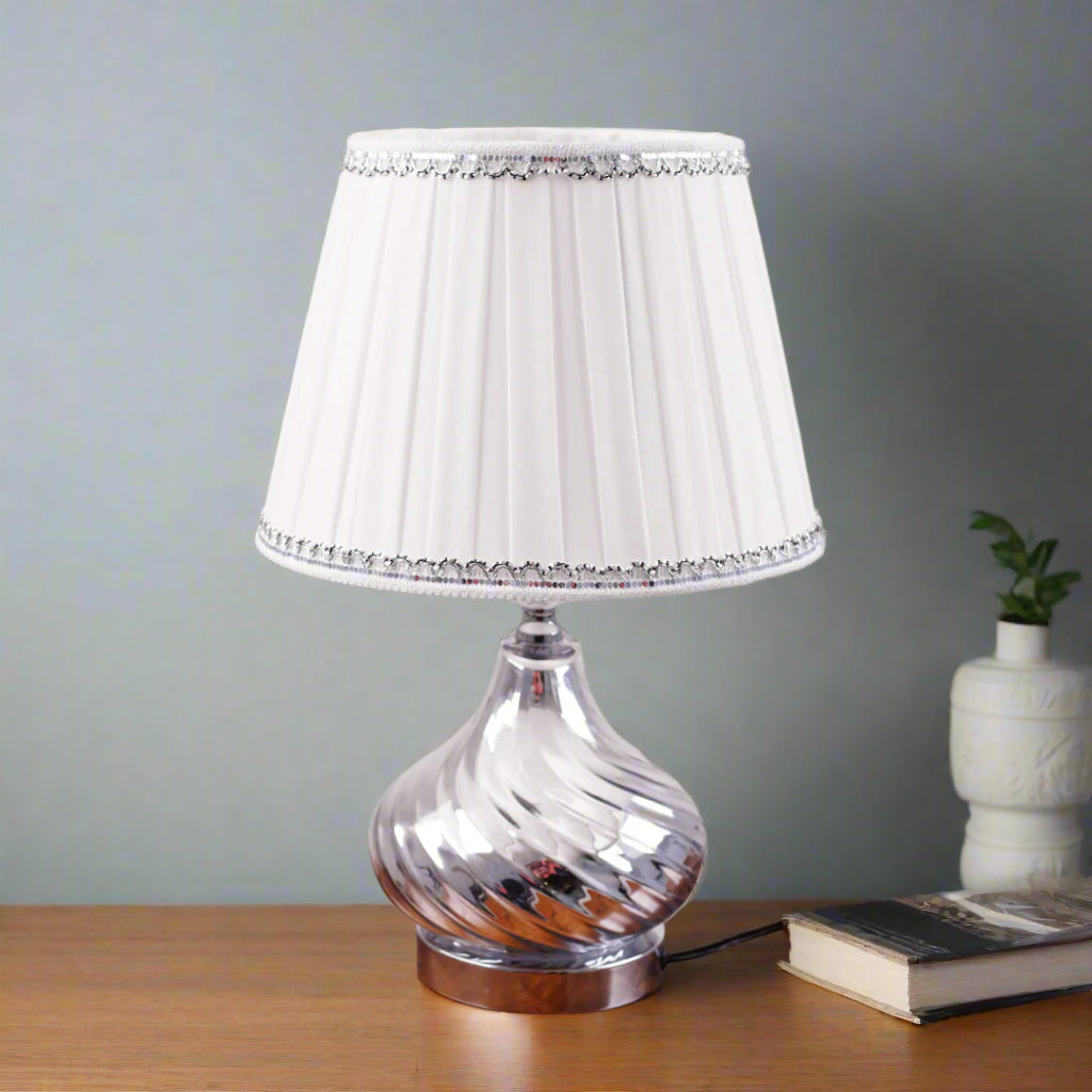 An elegant table lamp with a chic twisted silver base and a classic white lampshade. Equipped with an E27 LED light, it casts a warm and sophisticated glow.