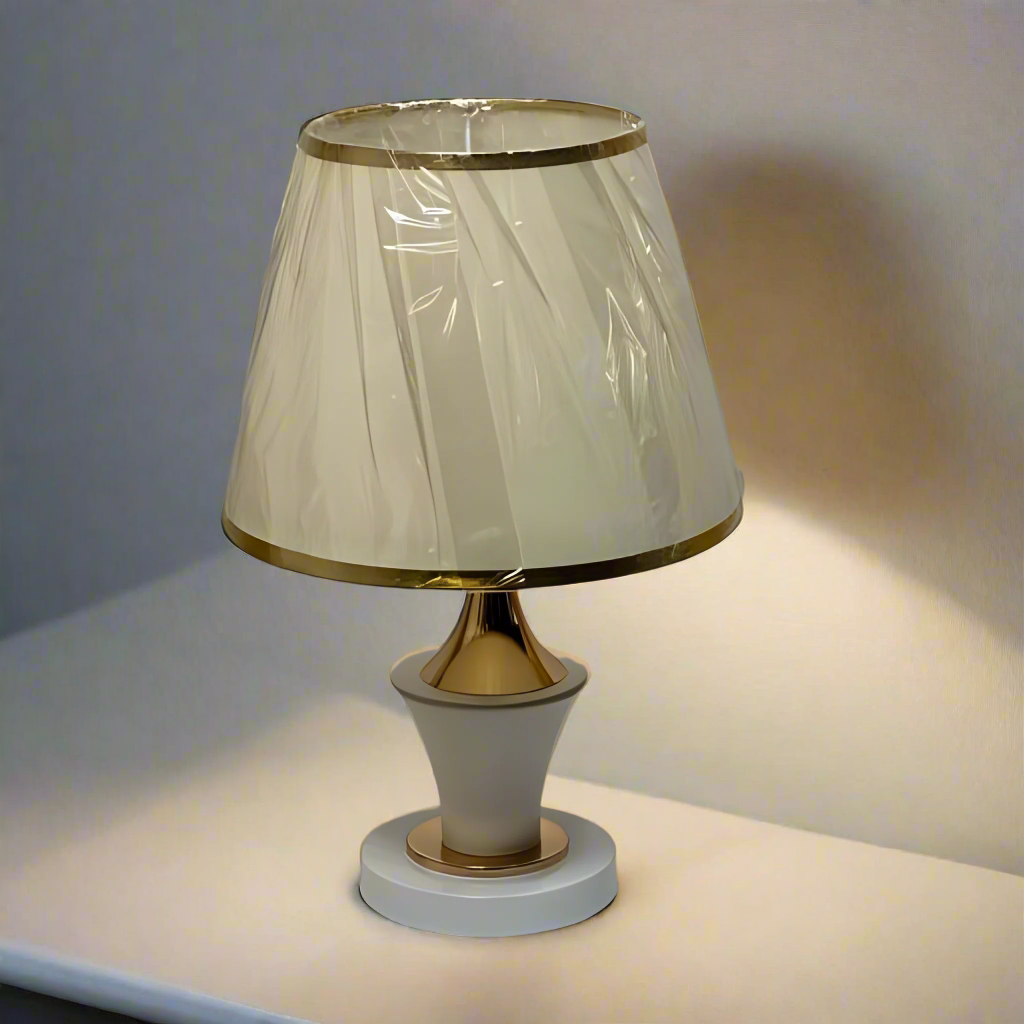 Modern white and gold table lamp with a flared lampshade and a sculpted curved base, placed on a white table.