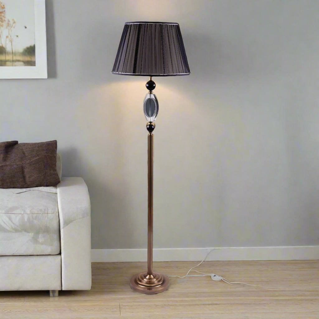 A tall, elegant floor lamp with a black lampshade, a golden stand, and black and crystal accents in the middle.
