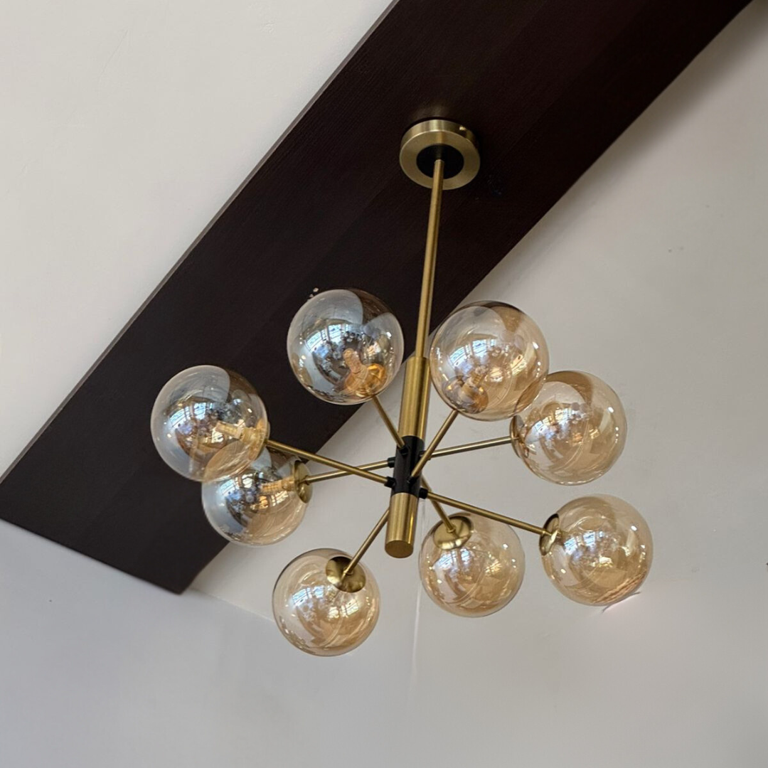 A gold chandelier with black accents, featuring multiple globe bulbs, mounted on a dark wooden beam