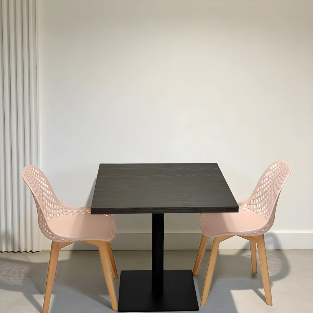 Black square table with two pink chairs against a white wall.