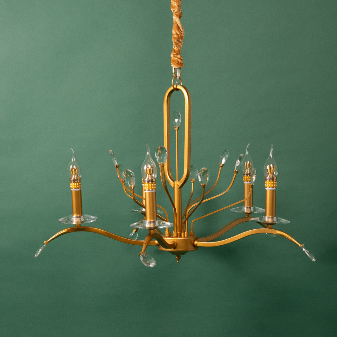 A vintage-inspired gold chandelier with delicate curved arms and candle-style bulbs, hanging against a green background.