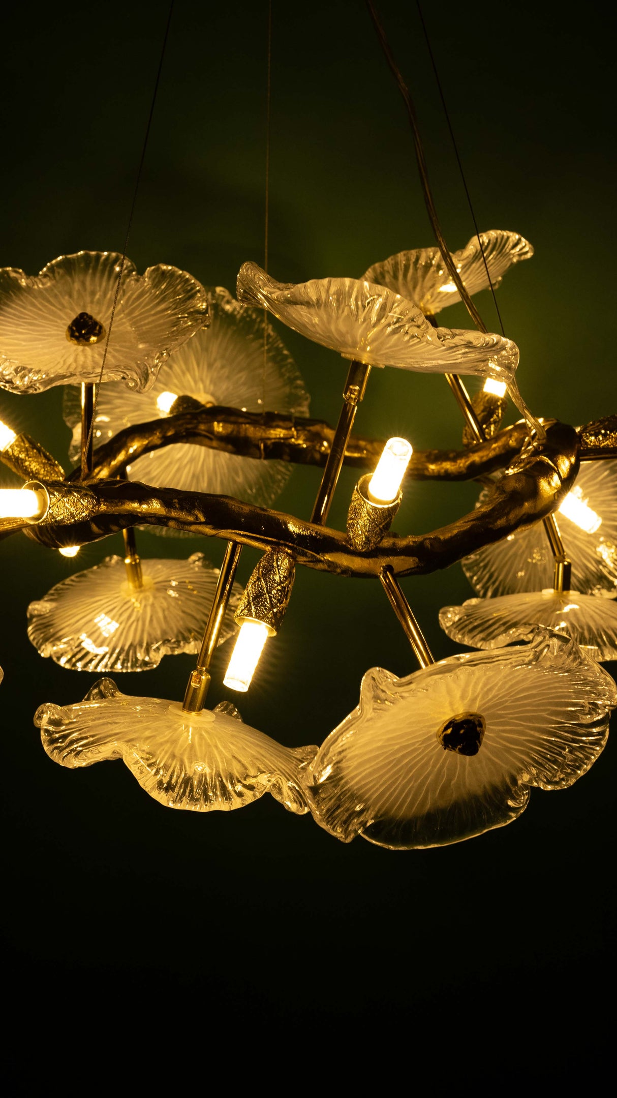 nature-inspired chandelier with golden branches and glass flower lampshades, glowing warmly against a dark green background.