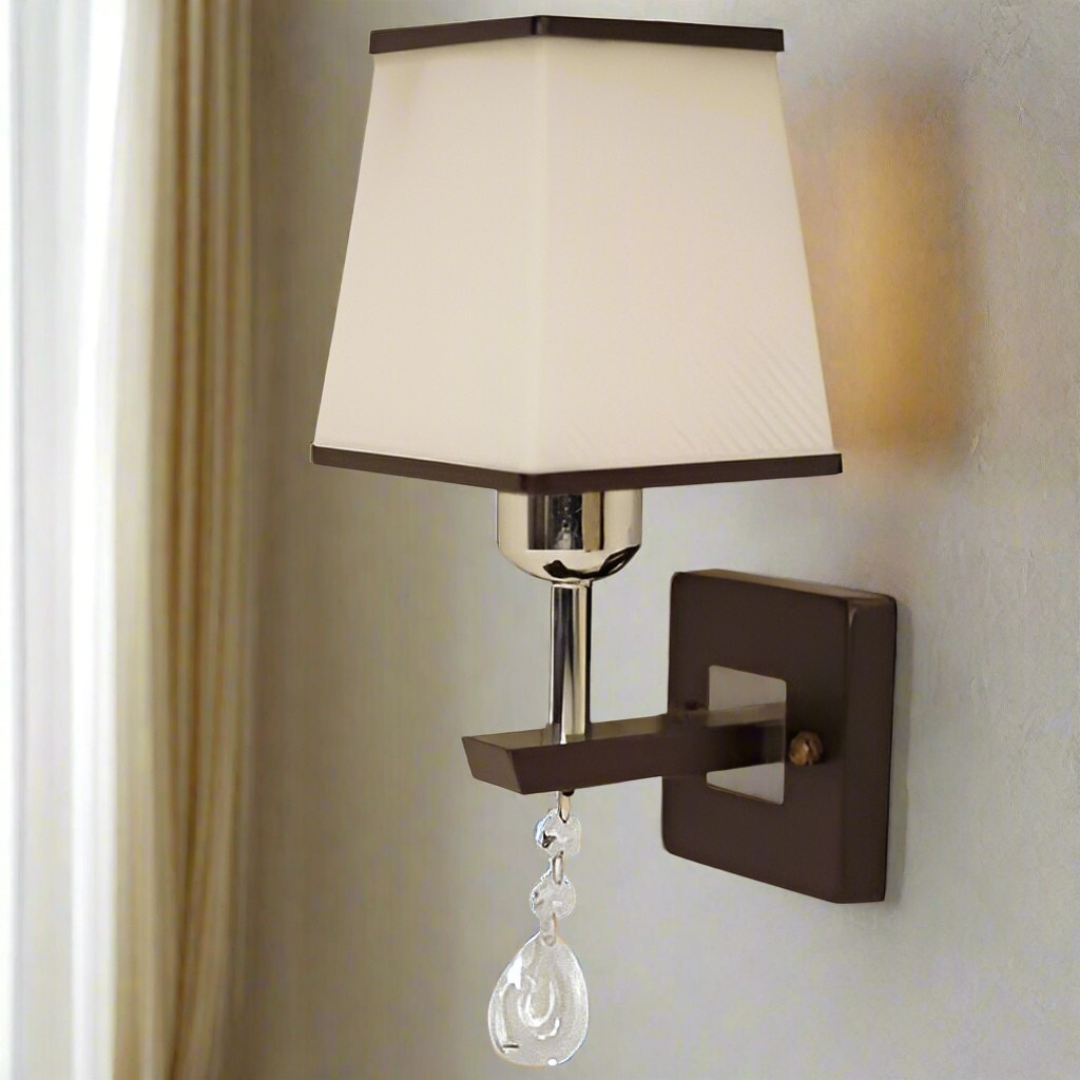 A brown and silver wall light with a rectangular fabric shade and a hanging crystal ornament, adding a touch of elegance.