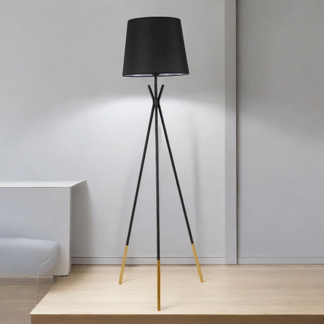 A black tripod floor lamp with wooden accents, standing on a light wooden platform against a white wall.