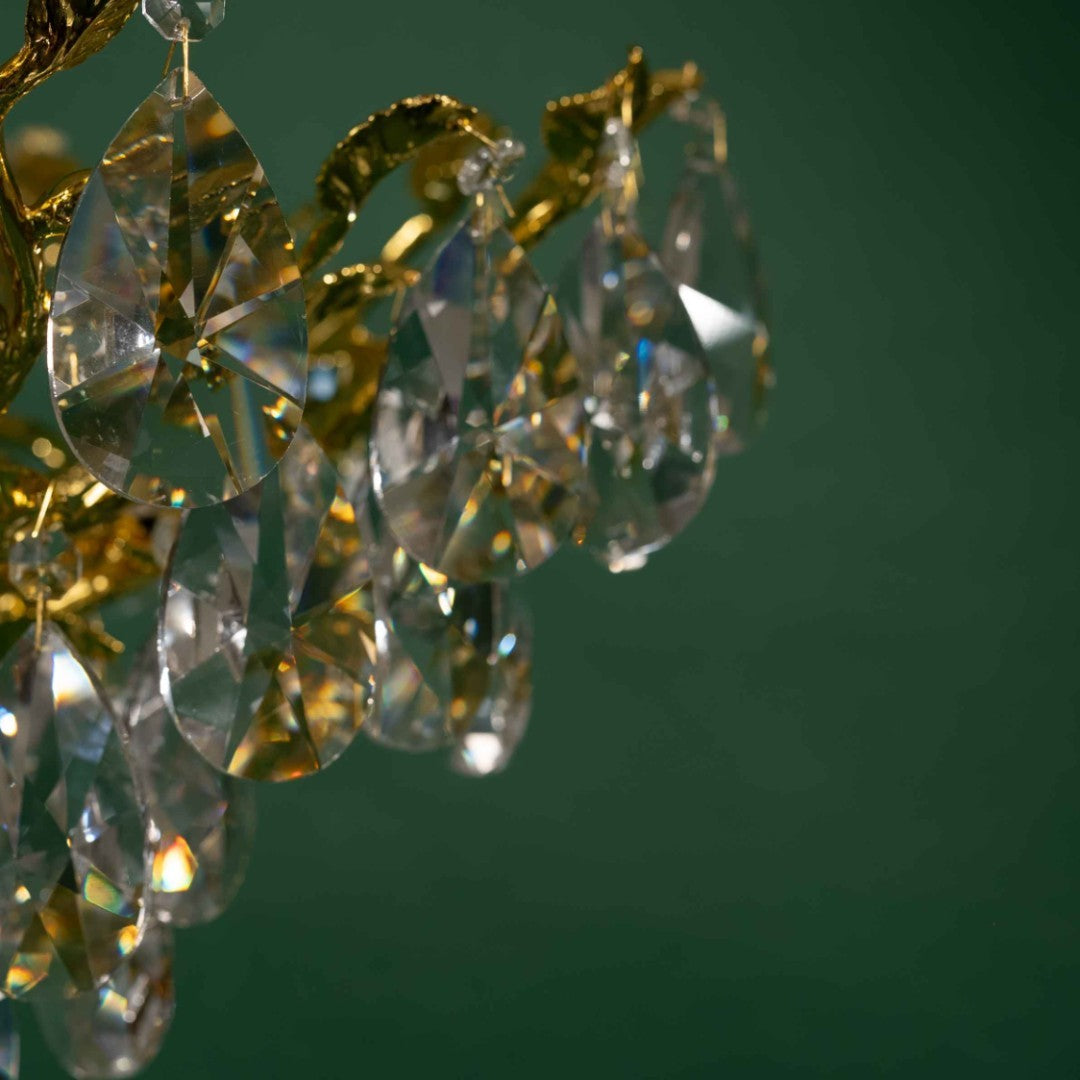 A close-up of a chandelier, focusing on the crystal drops, set against a green background.