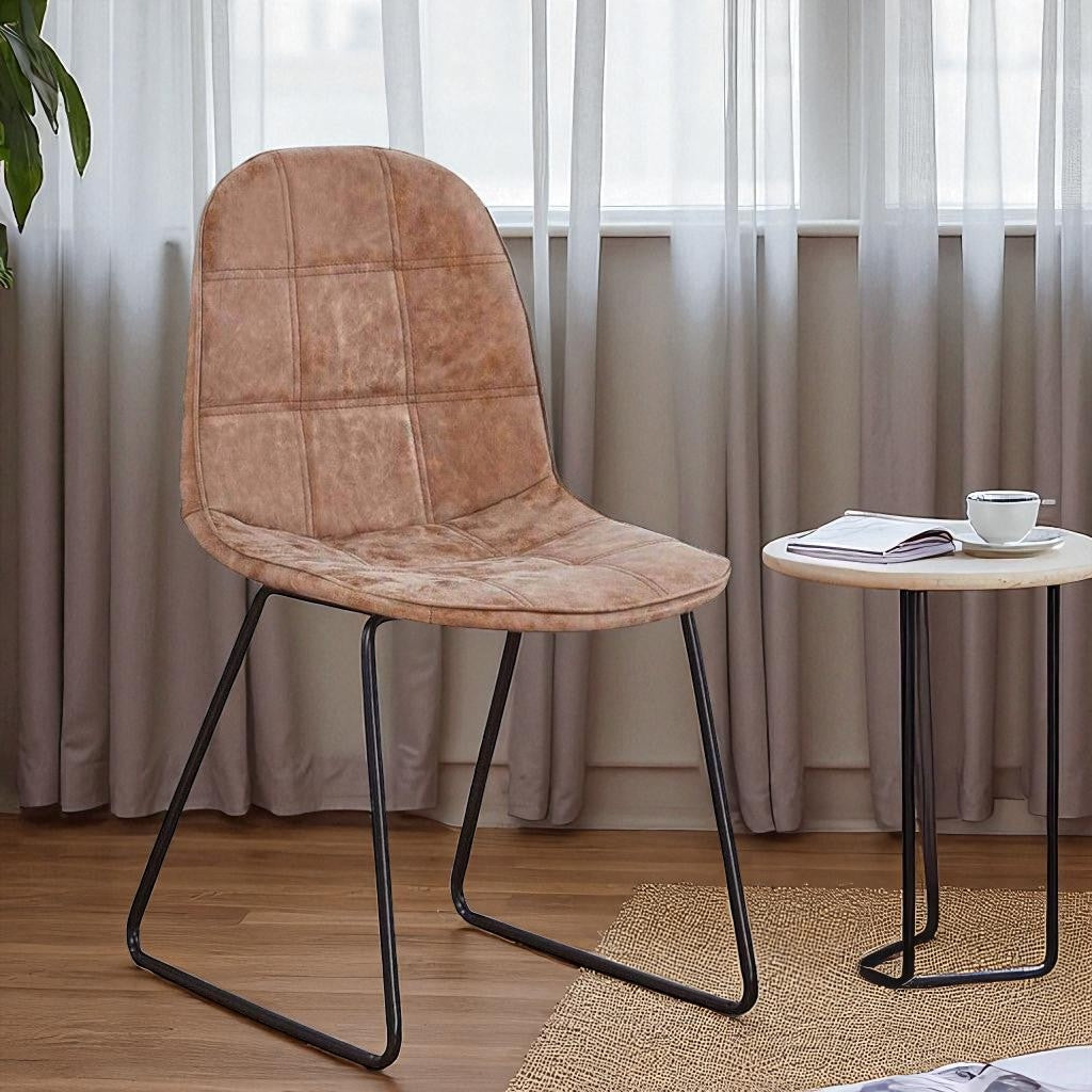 Brown leather chair with black metal legs in a room with curtains and a small table.