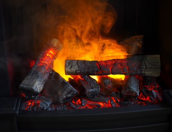 A close-up of a glowing electric fireplace with orange flames illuminating artificial logs.