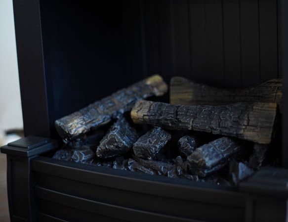 A close-up of artificial logs inside an electric fireplace, with slight illumination from the internal lighting.