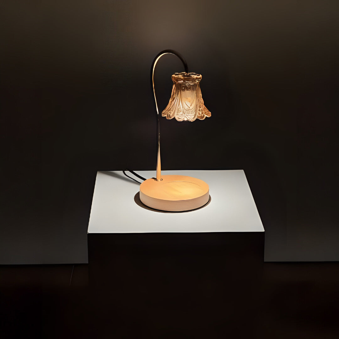 A vintage-inspired table lamp with a curved bronze arm holding a delicate bell-shaped glass shade, sitting on a round wooden base. Placed on a round white table.