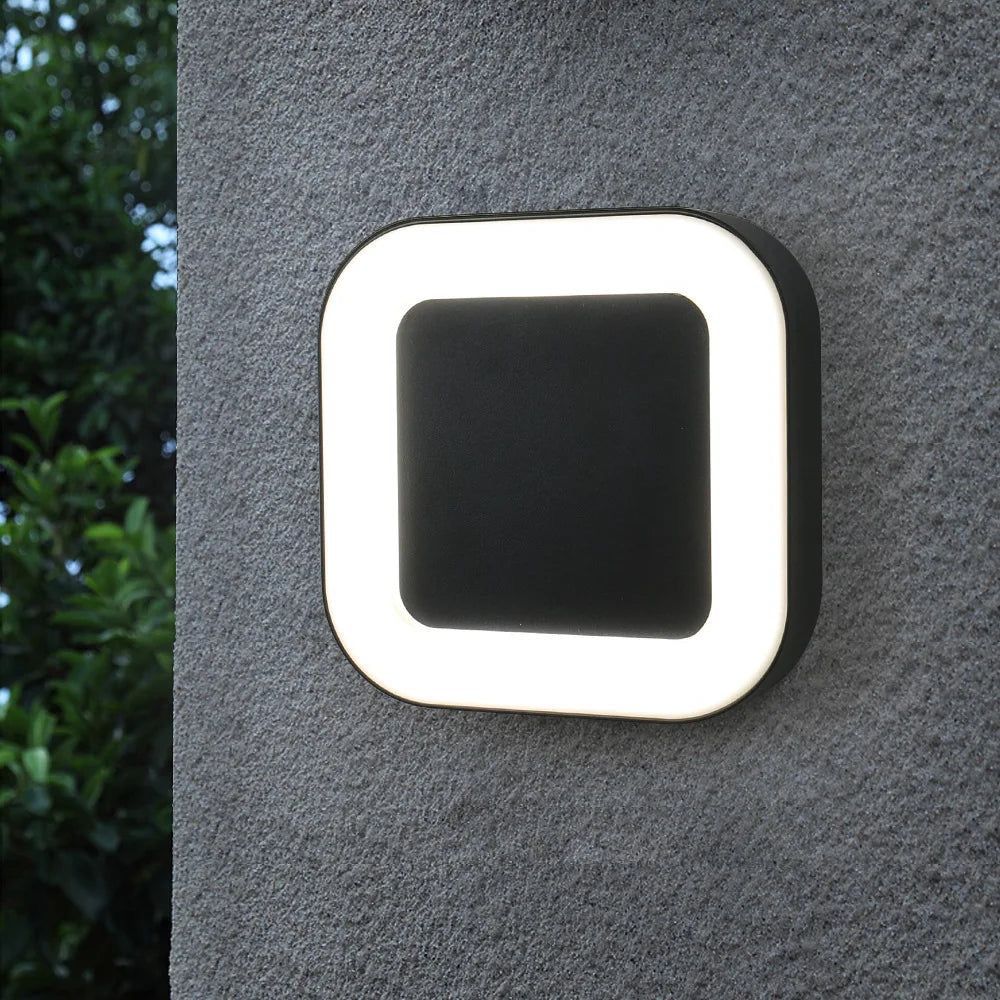 A modern outdoor wall light with a square black center and glowing white border, mounted on a dark exterior wall.