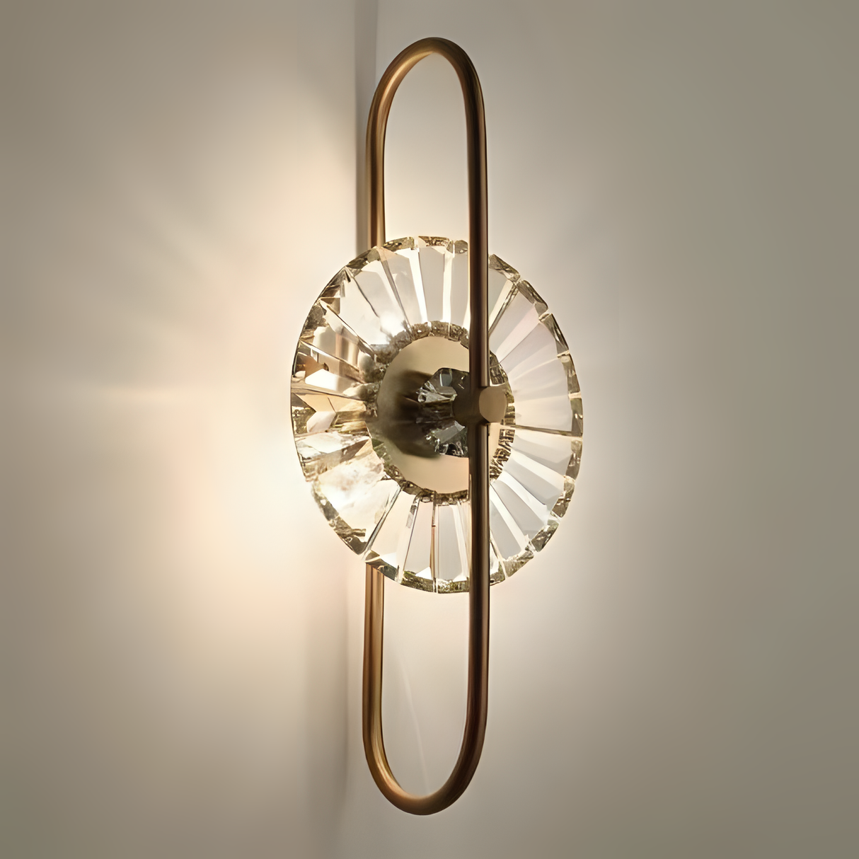 A modern gold wall sconce featuring an elongated oval frame with a central textured glass element, casting a soft, radiant glow.