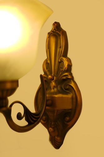 A close-up view of the decorative details on a gold wall sconce, highlighting intricate carvings and the frosted glass shade for a wall light.