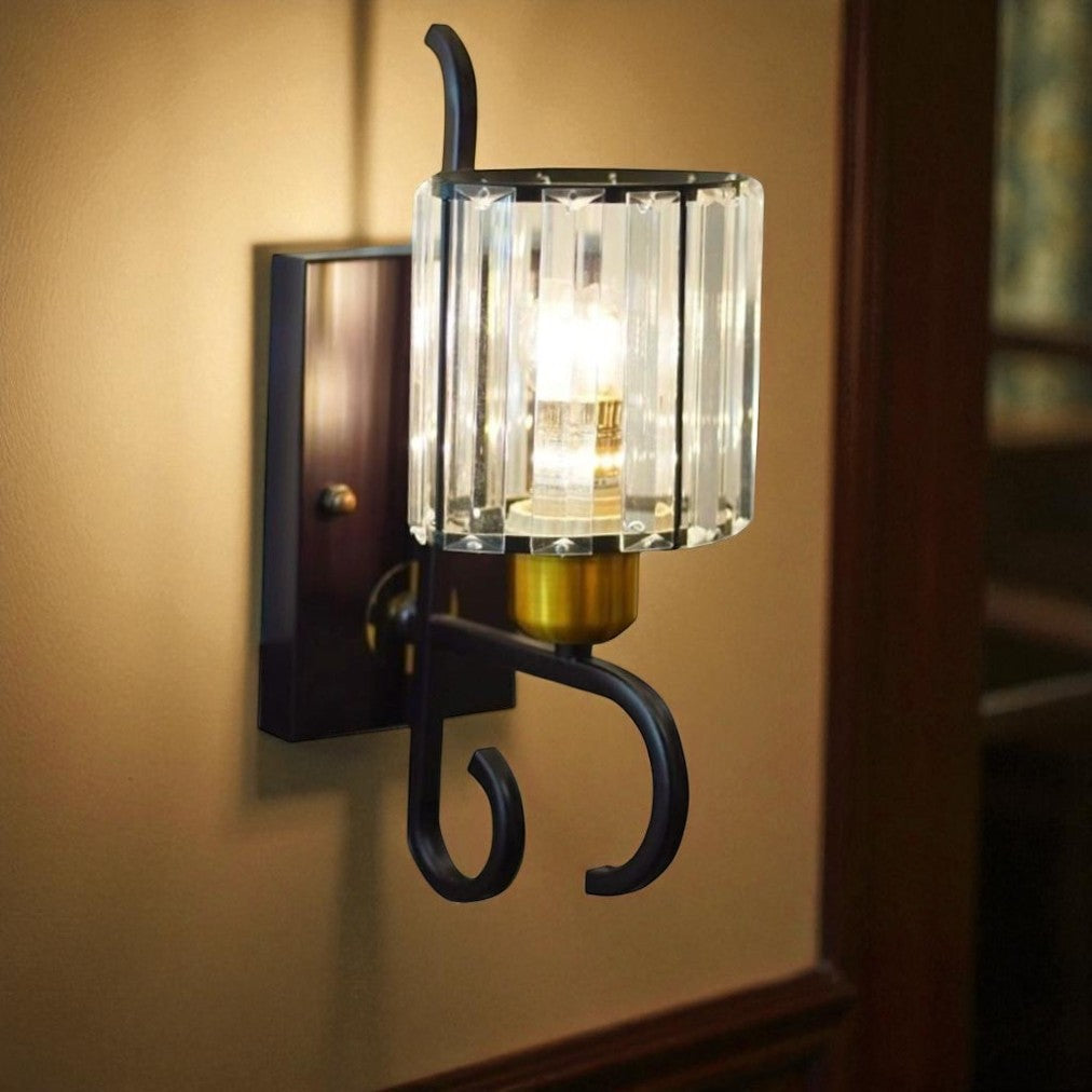 This stylish fixture features a brown metal base, a curved arm, and a cylindrical glass shade with gold accents on a marble wall. The lighting effect is soft and diffused.