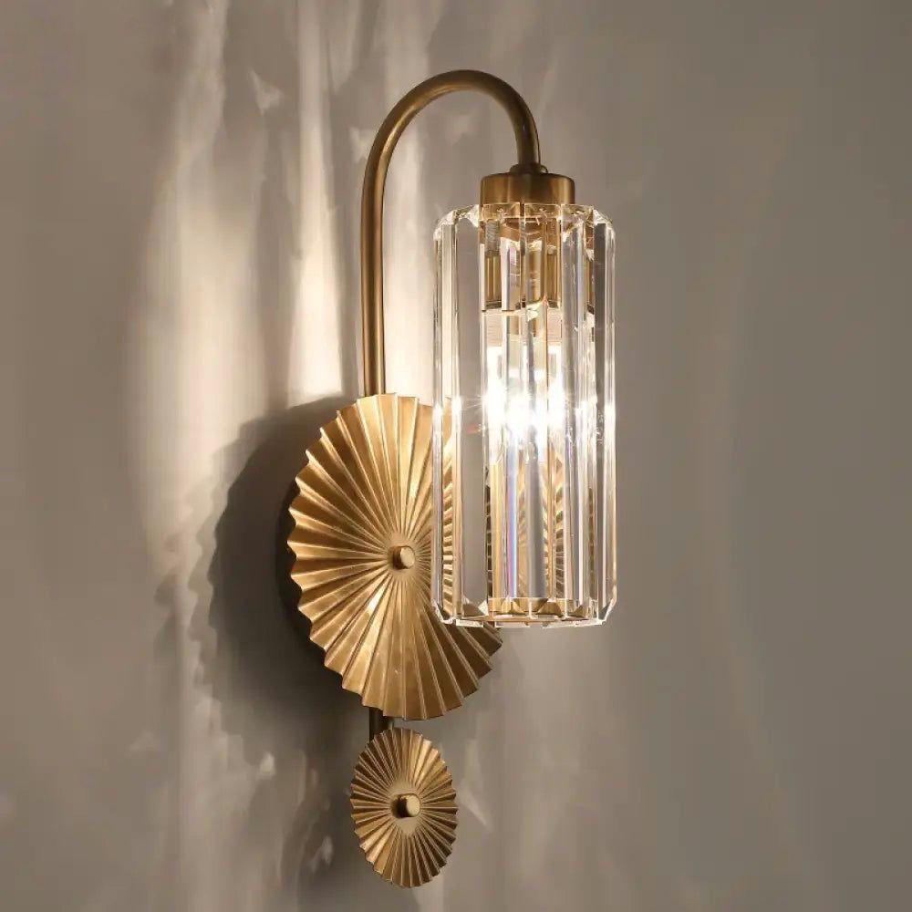 A gold and glass sconce with a unique ridged backplate and a vertically ribbed glass shade, mounted on a beige wall.