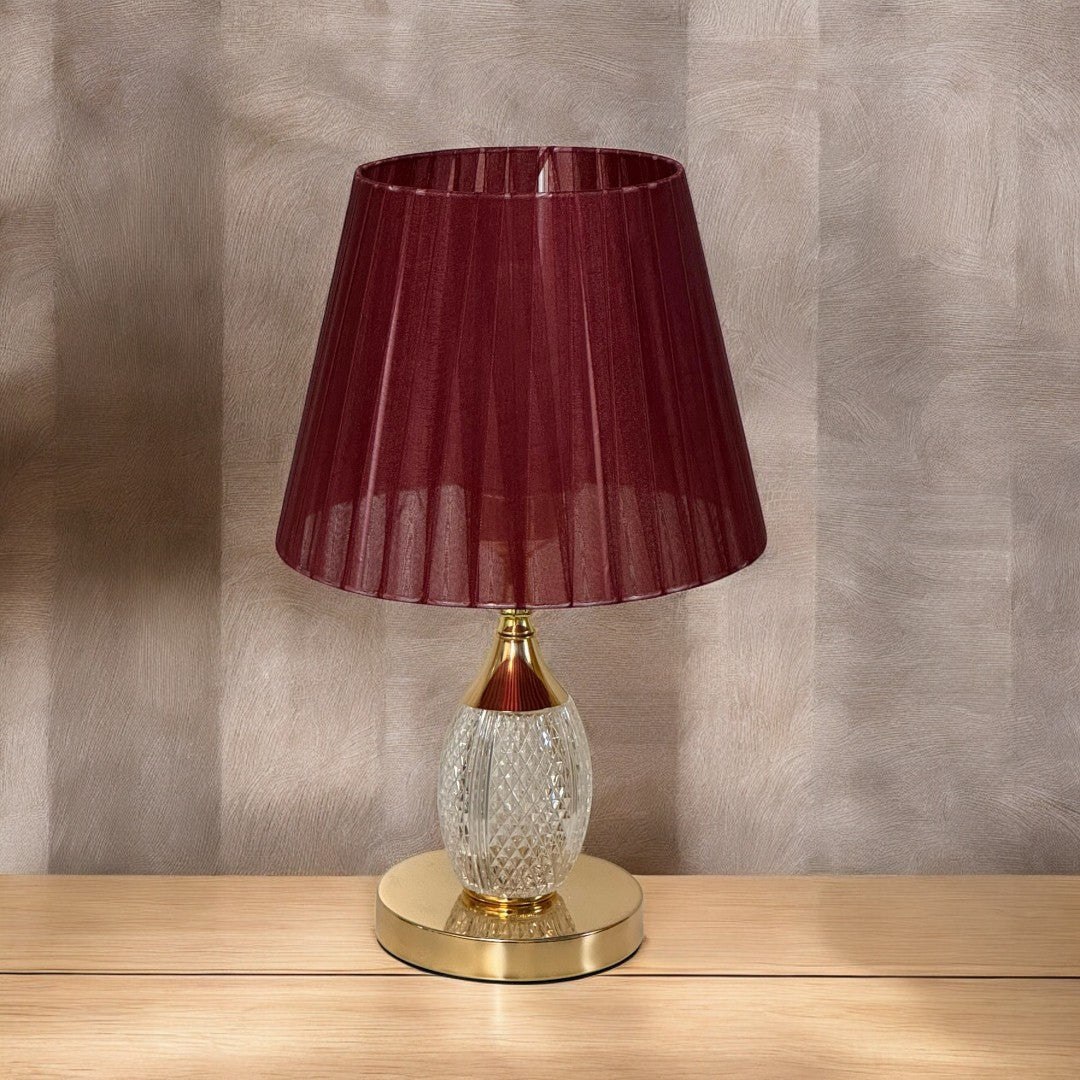 Traditional red and gold table lamp with a textured glass base and a deep red pleated shade, placed on a wooden table.