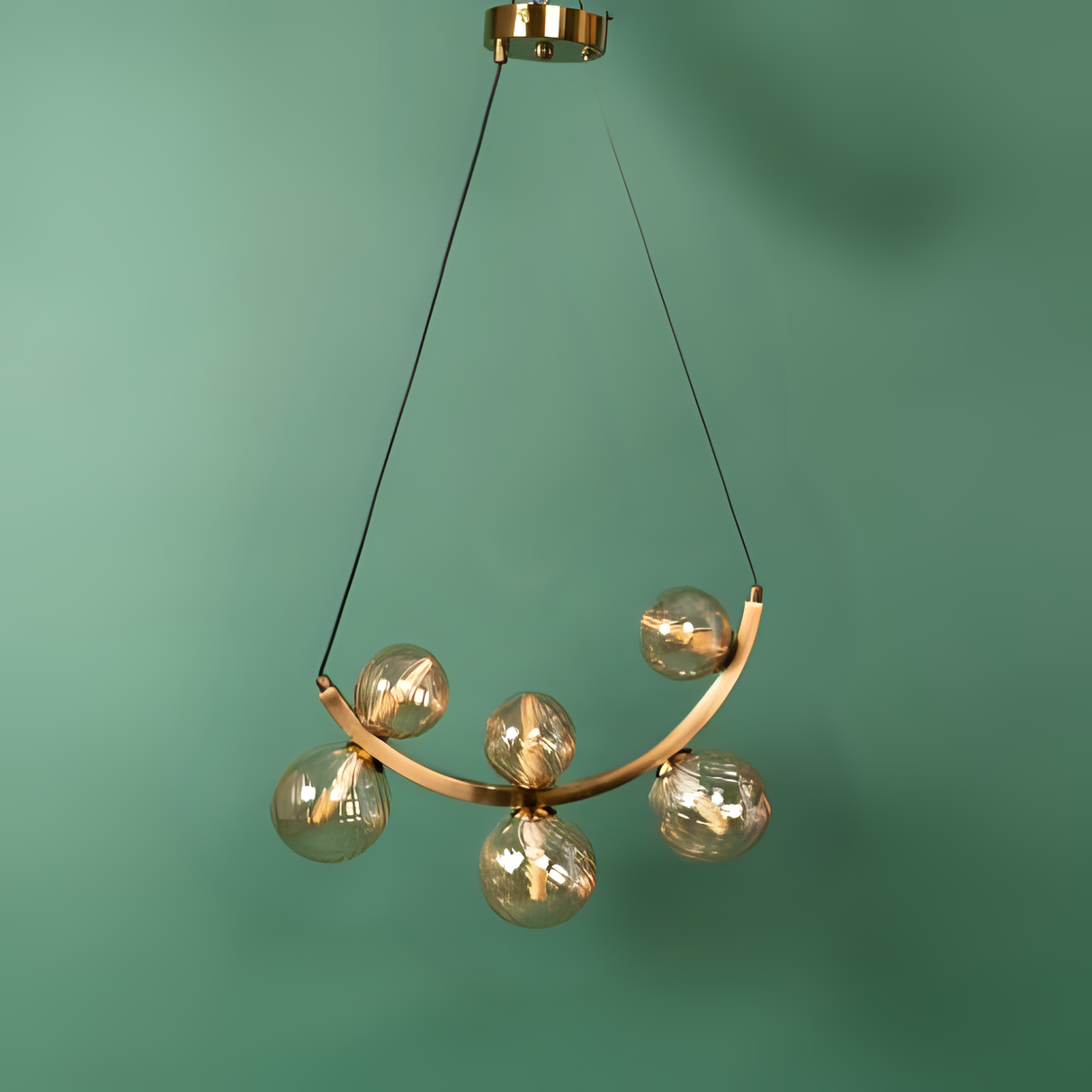 A curved gold chandelier with six glass globe lights, hanging against a green background.