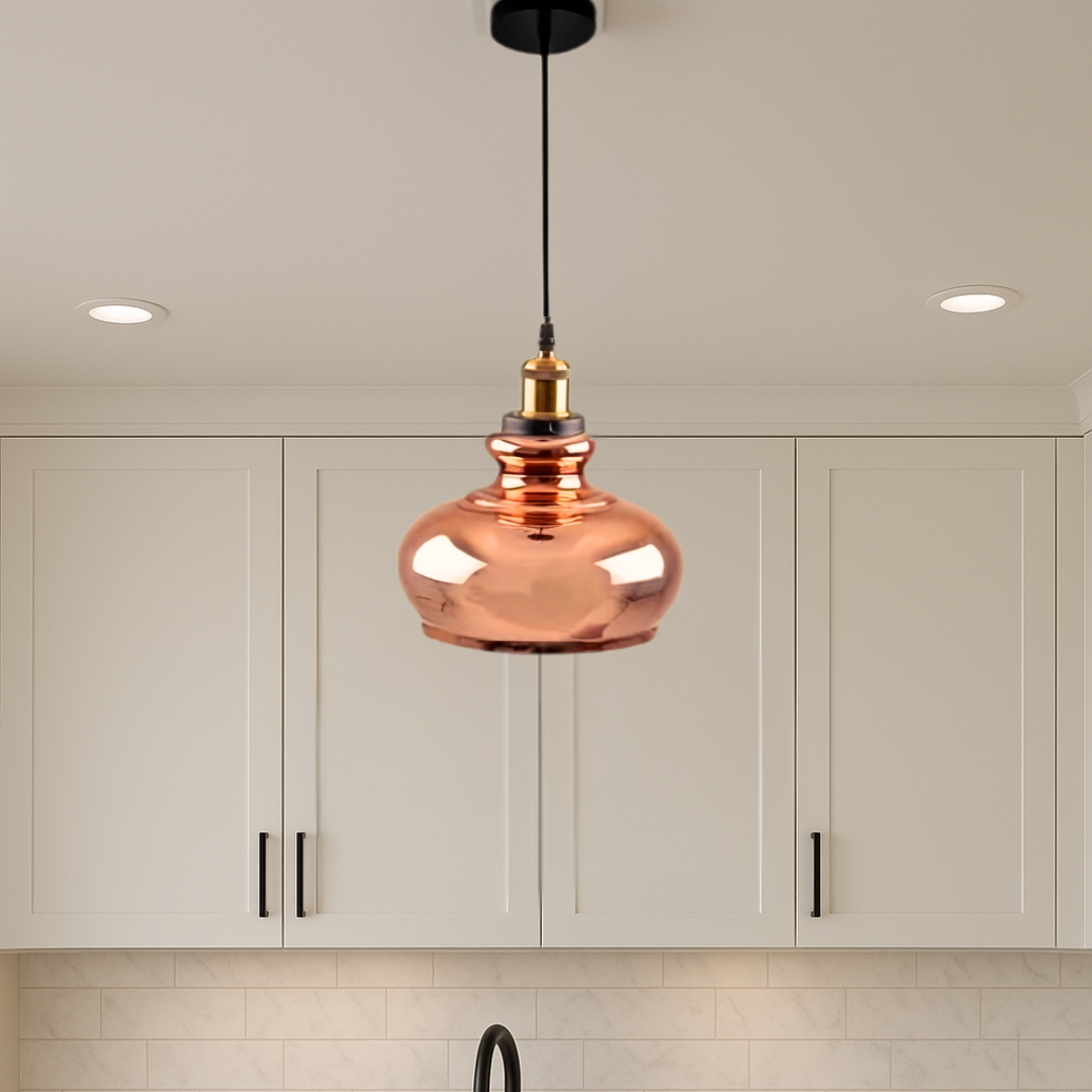 Copper pendant light hanging in a kitchen with white cabinets and tiled walls.