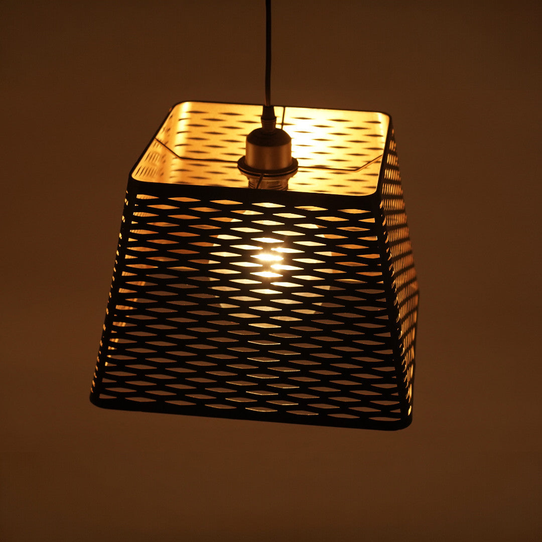 A warm-lit, black metal pendant light with a perforated, trapezoidal shade featuring a diamond mesh pattern, hanging from a black cord against a dark background.