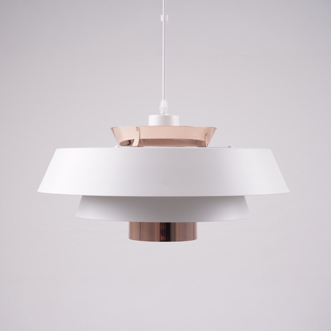 A modern layered pendant light with a matte white and copper finish, featuring a wide circular design with concentric discs, hanging from a black cord against a light gray background.