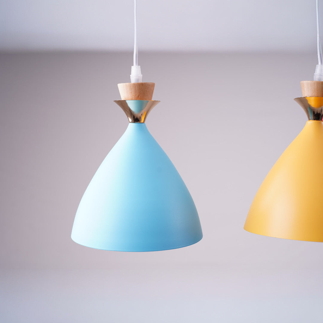 A close-up of two modern pendant lights with a smooth, conical design, one in pastel blue and the other in mustard yellow. Each light features a wooden and metallic accent near the top, with a white cord suspending them from the ceiling against a neutral background.