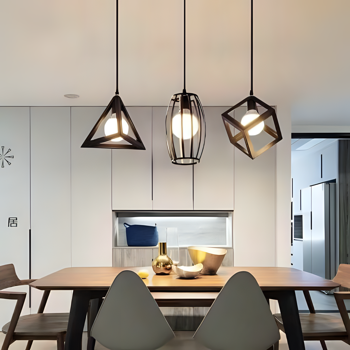 A trio of pendant lights with unique geometric metal frames in black and gold, suspended above a dining table in a contemporary open kitchen setting.