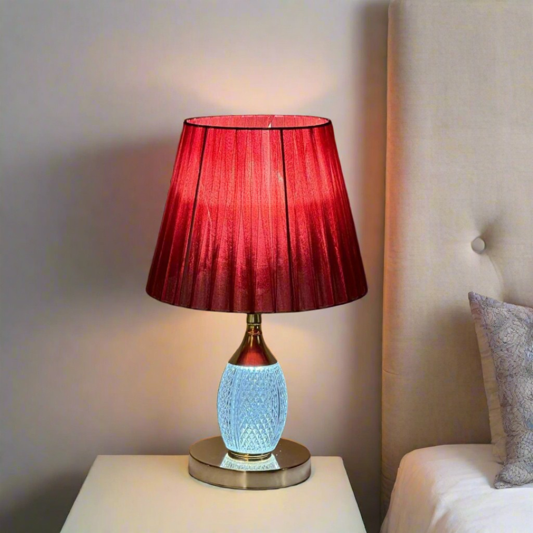 Bold red and gold table lamp with a striking red pleated lampshade equipped with an E27 LED bulb. The base features a gold finish with a built-in LED light inside the glass, adding a warm glow