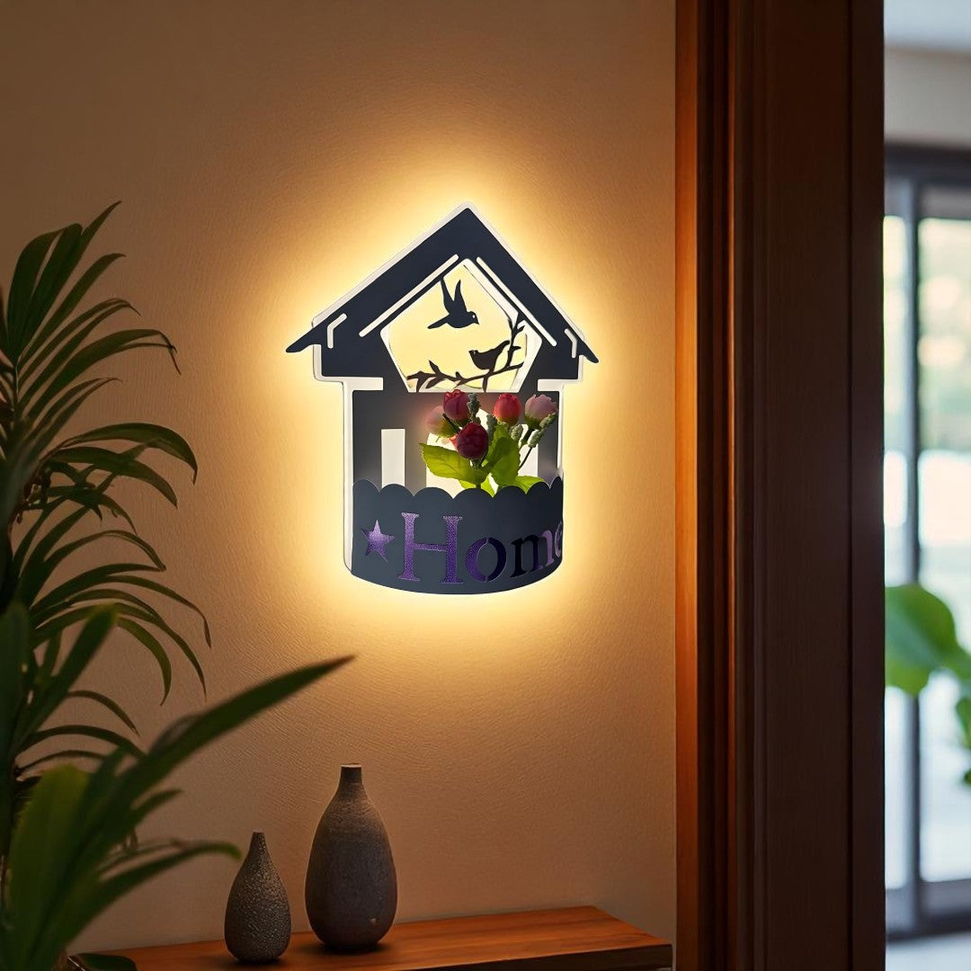 Wall-mounted LED light fixture designed in the shape of a white house , featuring a cork-style built-in compartment holding artificial pink and red tulip flowers. The light has a whimsical, cottage-inspired aesthetic and is mounted on a plain white wall.