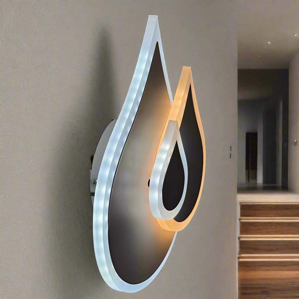 Wall-mounted LED light fixture shaped like two overlapping water droplets, with a soft white and warm white glow illuminating the surrounding wall.