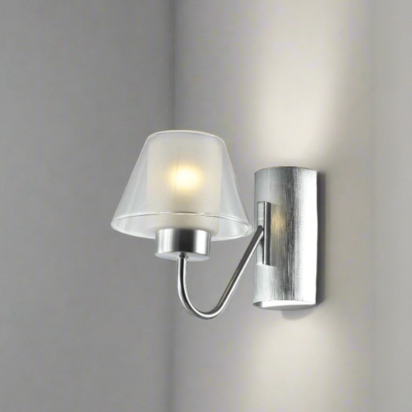 Modern wall-mounted sconce with a brushed metal base and a frosted glass lampshade emitting soft white light, installed on a light grey wall.