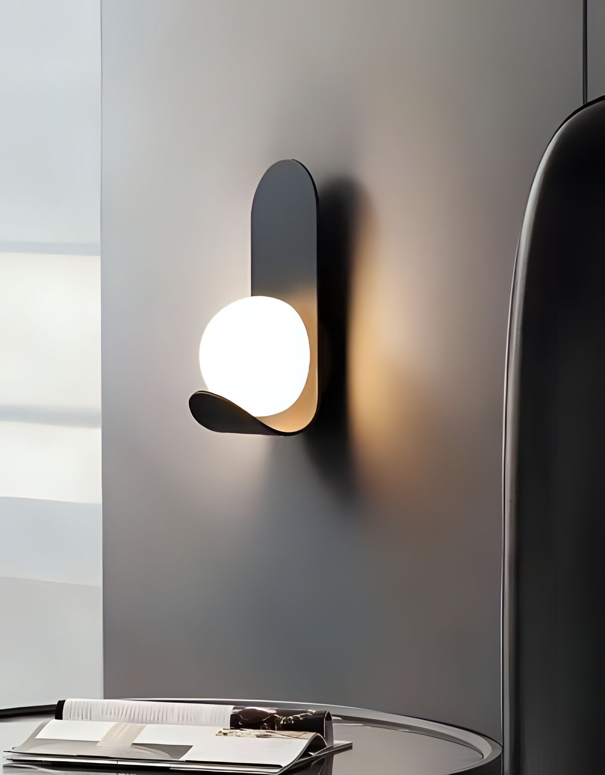 A modern black wall sconce with a vertically curved design, featuring a round frosted glass globe equipped with a LED lamp E27 that emits a soft warm glow.